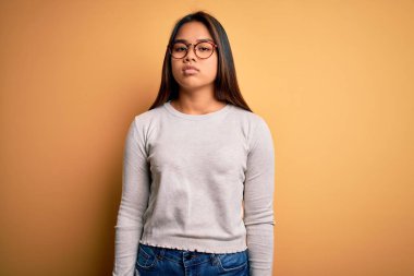 Sarı arka planda günlük süveter ve gözlük takan genç, güzel Asyalı kız yüzünde ciddi bir ifadeyle rahatladı. Basit ve doğal bir şekilde kameraya bakıyorsun..