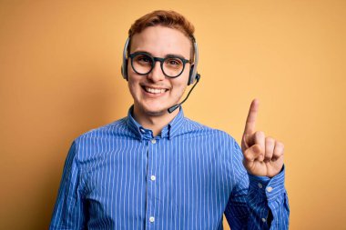 Gözlüklü, genç, kızıl saçlı çağrı merkezi ajanı başarılı bir fikir için kulaklık kullanıyor. Heyecanlı ve mutlu. Bir numara..