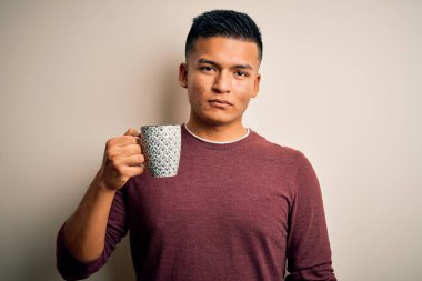 Genç, yakışıklı, Latin bir adam izole edilmiş beyaz arka planda bir fincan kahve içiyor.