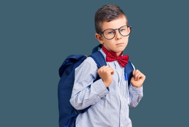 Sevimli sarışın çocuk inek papyonu takıyor ve sırt çantası takıyor. Düşünme tavrı takınıyor ve kendine güveni tam görünüyor. 