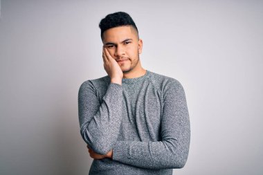 İzole edilmiş beyaz arka plan üzerinde duran sıradan bir süveter giyen genç, yorgun ve bunalımda kollarını kavuşturmaktan sıkılmış bir adam..