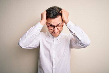 Gözlük takan genç yakışıklı iş adamları ve izole edilmiş arka plan üzerine şık gömlekler. Ağrı ve migren yüzünden çaresiz ve stresli bir baş ağrısı. Ellerini başının üstüne koy..