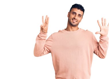 Gündelik kıyafetler giyen genç İspanyol adam sekiz numarayı gösterip işaret ederken kendinden emin ve mutlu bir şekilde gülümsüyor.. 