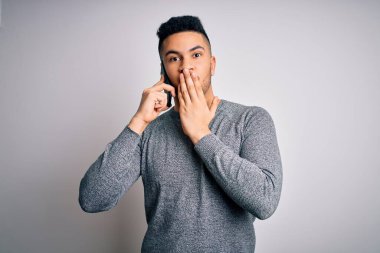 Genç yakışıklı bir adam beyaz arka planda akıllı telefondan konuşuyor. Ağzı kapalı, utancından ağzı açık, korkudan ağzı açık, sessizlikten korkan, gizli bir kavram.