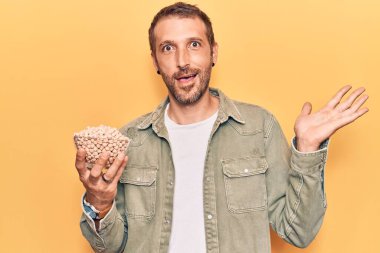 Genç yakışıklı adam elinde nohut kasesi tutarak başarıyı mutlu bir gülümsemeyle kutluyor ve kazanan el kaldırarak ifade ediyor. 