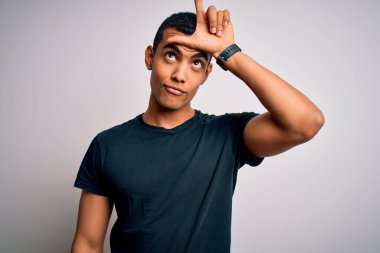 Genç, yakışıklı, Afro-Amerikalı, sıradan tişörtler giyen, beyaz arka planda dikilen, parmakları alnında insanlarla alay eden ezik jestler yapan, alay eden, aşağılayan bir adam..