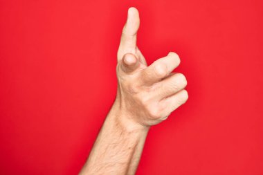İzole edilmiş kırmızı arka planda parmaklarını gösteren, kameraya işaret eden, yönü seçen ve işaret eden beyaz bir genç adam.