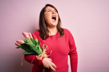 Güzel ve cüsseli bir kadın pembe arka planda romantik laleler tutuyor kızgın ve öfkeli çığlıklar atıyor, öfkeyle bağırıyor. Öfke ve agresif kavram.
