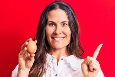 Güzel esmer iş kadını elinde bir deste dolarla kırmızı arka planda gülümsüyor.