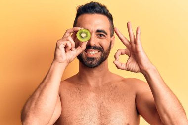 İspanyol asıllı genç üstsüz bir adam kivi tutuyor. Parmaklarıyla imza atıyor, gülümsüyor ve mükemmel bir sembol oluşturuyor. 