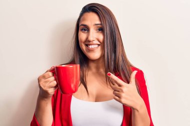 Genç, güzel, esmer kadın kahve fincanı içiyor. Gülümsüyor, mutlu bir şekilde işaret ediyor. 