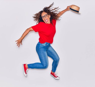 Orta yaşlı, güzel İspanyol bir kadın günlük kıyafetler giyiyor ve mutlu gülümsüyor. Yüzünde tebessümle beyaz arka planda şapkayla zıplıyor