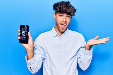 Kırık akıllı telefon tutan genç İspanyol adam mutluluğu kutlayan kırık bir ekran ve kaldırılmış bir el ile kazanan yüz ifadesi sergiliyor. 