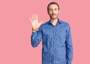 Gündelik kıyafetler giyen genç yakışıklı adam beş numarayı gösterip işaret ederken kendinden emin ve mutlu bir şekilde gülümsüyor.. 