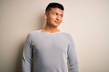 Genç, yakışıklı, sıradan bir süveter giyen, izole edilmiş beyaz arka planda duran, gülümseyen ve düşüncelere dalan Latin bir adam..