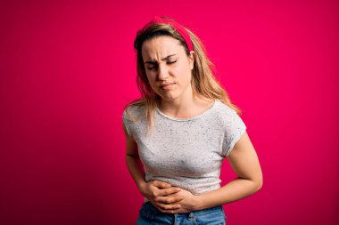 Genç, güzel, sarışın bir kadın, rahat olmayan pembe arka planda duran, hazımsızlık ve acı veren bir hastalıktan dolayı el üstünde duran, gündelik bir tişört giyiyor. Ache kavramı.