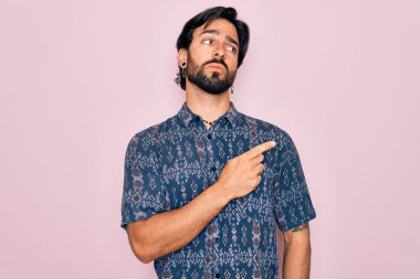 Pembe arka planda hippi tarzı giyinmiş genç, Latin asıllı bohem bir adam. Elleriyle reklamını yapıyor, ciddi ve sakin bir yüz ifadesi var.