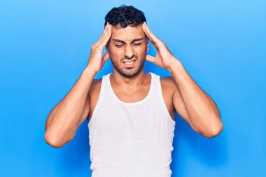Latin asıllı genç bir adam elleri kafasında günlük kıyafetler giyiyor, stres yüzünden baş ağrısı çekiyor. migren ağrısı. 