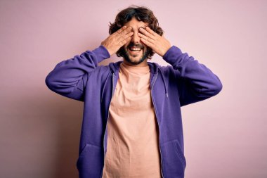 Genç, yakışıklı, sakallı, pembe arka planda sıradan bir kazak giyen, elleri gülücüklü, neşeli ve eğlenceli gözleri olan yakışıklı bir adam. Kör kavram.