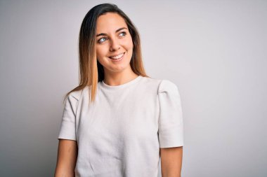 Mavi gözlü, beyaz arka planda sıradan tişörtler giyen, yüzünde gülümseme, doğal bir ifade olan genç, güzel sarışın bir kadın. Kendinden emin gülen.
