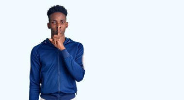 Genç Afro-Amerikan erkek spor giysisi giyiyor ve parmakları dudaklarında sessiz olmak istiyor. sessizlik ve gizli konsept. 