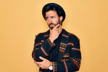 Genç, yakışıklı, bohem, hippi tarzı ve bohem şapkalı bir adam. Bir soru hakkında endişeleniyor. Endişeli ve gergin.