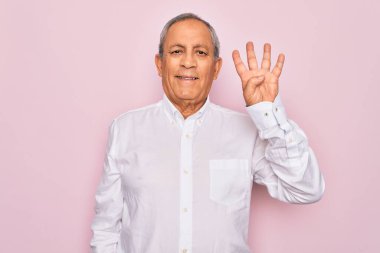 Üst düzey yakışıklı, gri saçlı, zarif tişörtlü, soyutlanmış pembe arka planda dört numarayı gösterirken, kendinden emin ve mutlu bir şekilde gülümsüyor..