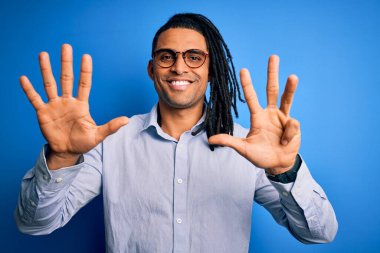 Rastgele gömlek ve gözlük takmış genç, Afro-Amerikalı adam dokuz numarayı gösterip gösterirken kendinden emin ve mutlu gülümsüyor..