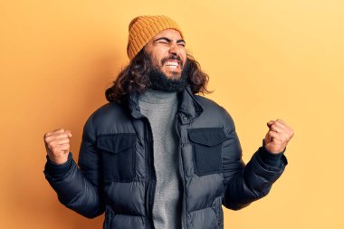 Gündelik kışlık giysiler giyen genç bir Arap. Çok mutlu ve heyecanlı. Kolları havada, gülümseyen ve başarı için çığlık atan kazanan bir jest yapıyor. kutlama konsepti. 