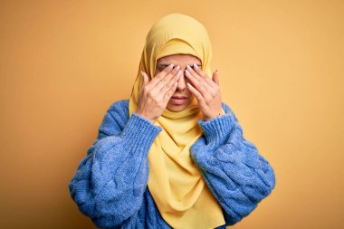 Genç, güzel, esmer, Müslüman kadın izole edilmiş sarı arka plan üzerine Arap başörtüsü takıyor. Yorgunluk ve baş ağrısı için gözlerini ovuşturuyor, uykulu ve yorgun bir ifade takınıyor. Görüş sorunu