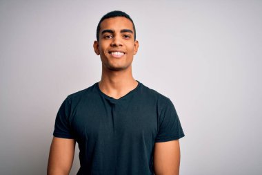 Genç, yakışıklı, Afro-Amerikan bir adam günlük tişörtler giyip beyaz arka planda mutlu ve havalı bir gülümsemeyle dikiliyor. Şanslı kişi..