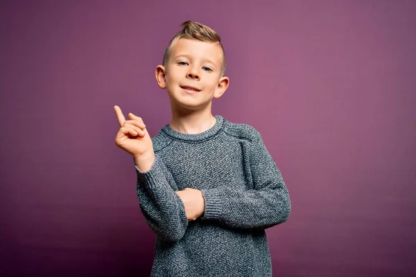 코카서스 아이가 스웨터를 보라색 웃으며 손가락으로 카메라를 봅니다 — 스톡 사진