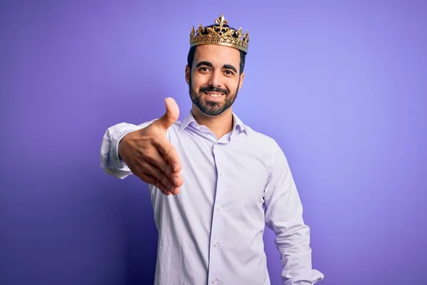 年轻英俊的男人 留着金色的胡须 头戴紫色背景的王冠 微笑友好地握手表示问候和欢迎 成功的业务 — 图库照片