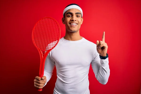 若いですハンサムなアフリカ系アメリカ人スポーツマン遊びテニスを使用してラケット以上赤背景驚きでアイデアや質問を指差す指で幸せな顔 ナンバーワン — ストック写真