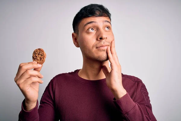 Jovem Hispânico Comendo Biscoito Chocolate Sobre Fundo Isolado Rosto Sério — Fotografia de Stock