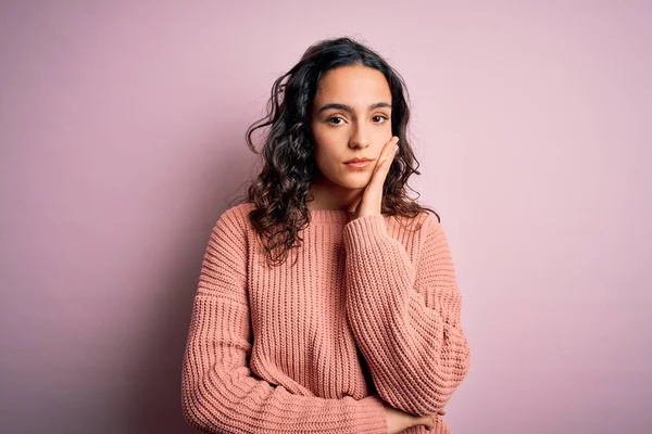 Young beautiful woman with curly hair wearing casual sweater over isolated pink background thinking looking tired and bored with depression problems with crossed arms.