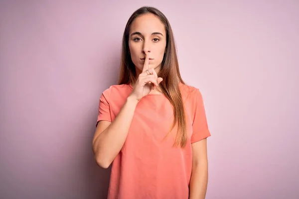 孤立したピンクの背景の上に立つカジュアルなTシャツを着た若い美しい女性は 唇に指で静かになるように求めています 沈黙と秘密の概念 — ストック写真