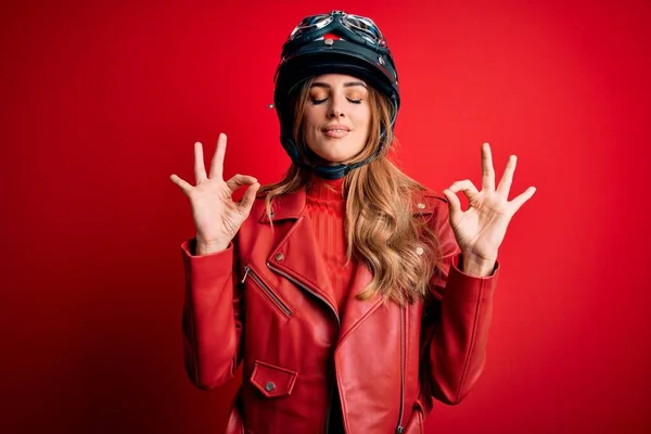 赤い背景の上に元ヘルメットを身に着けている若い美しいブルネットのオートバイの女性は 指で瞑想のジェスチャーをして閉じて目でリラックスして笑顔 ヨガのコンセプト — ストック写真