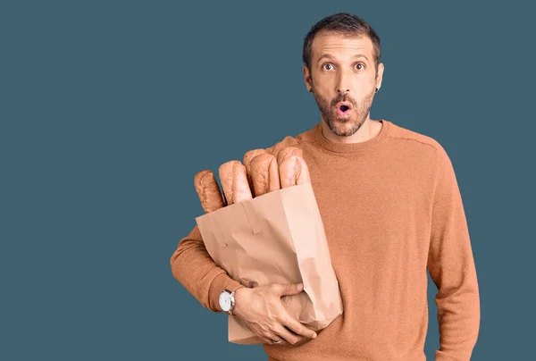 Junger Gutaussehender Mann Hält Papiertüte Mit Brot Der Hand Erschrocken — Stockfoto
