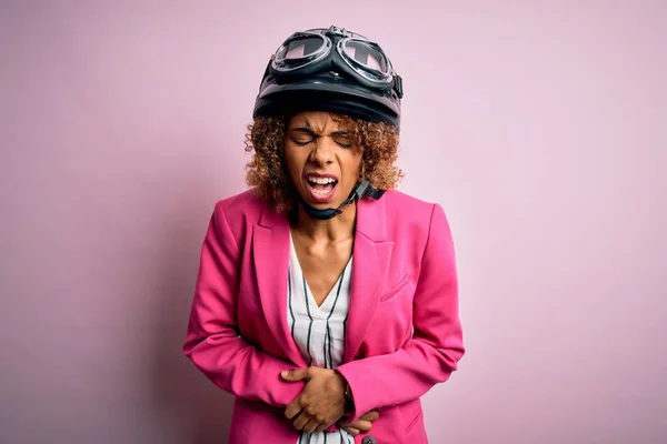 非洲裔美国骑摩托车的妇女 卷曲的头发 头戴安全帽 粉色背景 双手放在肚子上 因为恶心 痛苦的疾病感觉不舒服 阿切概念 — 图库照片