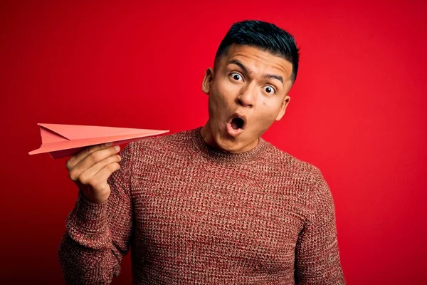 Joven Hombre Latino Guapo Sosteniendo Avión Papel Sobre Fondo Rojo —  Fotos de Stock