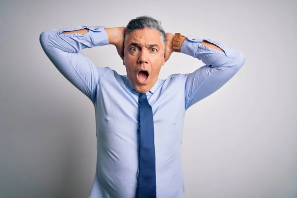 Middle age handsome grey-haired business man wearing elegant shirt and tie Crazy and scared with hands on head, afraid and surprised of shock with open mouth