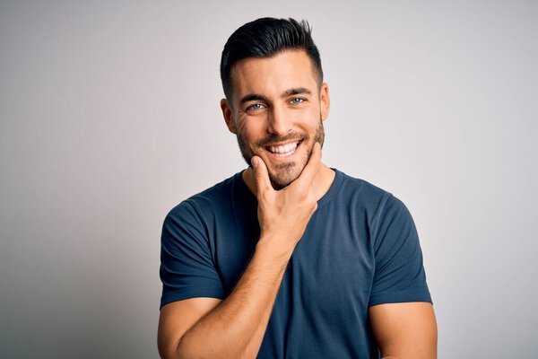 Young handsome man wearing casual t-shirt standing over isolated white background looking confident at the camera smiling with crossed arms and hand raised on chin. Thinking positive.