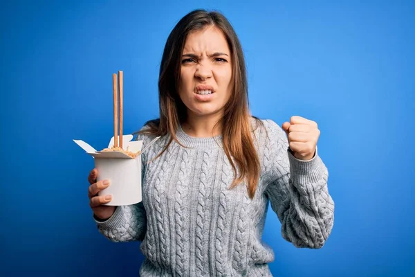 年轻的女人吃着亚洲面 用筷子在蓝色的背景上端走盒子 她生气得大叫 生气得发疯 怒气冲冲 — 图库照片