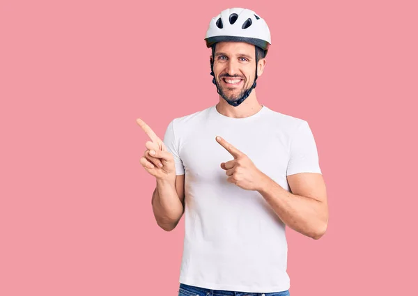 Young handsome man wearing bike helmet smiling and looking at the camera pointing with two hands and fingers to the side.