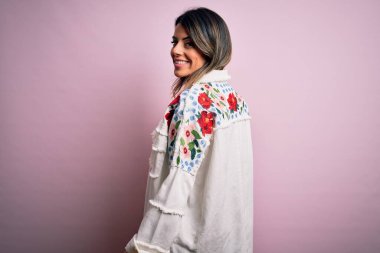 Moda kıyafetleri giyen genç ve güzel bir kadın. Manken, sokak tarzı giyiniyor. Pembe arka planda dikiliyor.