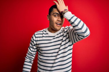 İzole edilmiş kırmızı arka planda dikilen sıradan çizgili tişört giyen genç Brezilyalı bir adam hata sonucu el ele tutuşarak şaşırdı. Hatayı hatırla. Unuttum, kötü hafıza konsepti.