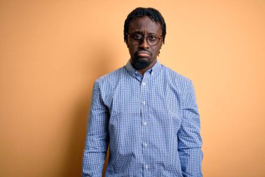 Sarı arka planda gömlek ve gözlük takan yakışıklı Afro-Amerikalı genç adam depresif ve endişeli, sinirli ve korkmuş. Üzücü ifade.