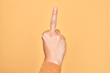 Hand of caucasian young man showing fingers over isolated yellow background showing provocative and rude gesture doing fuck you symbol with middle finger