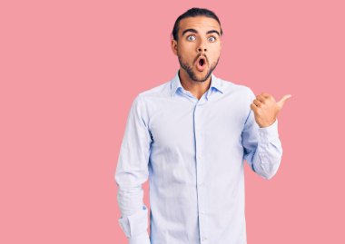 İş kıyafetleri giyen genç yakışıklı adam, elleri yana doğru işaret ederek şaşırdı, ağzı açık şaşkın bir şekilde ifade verdi.. 